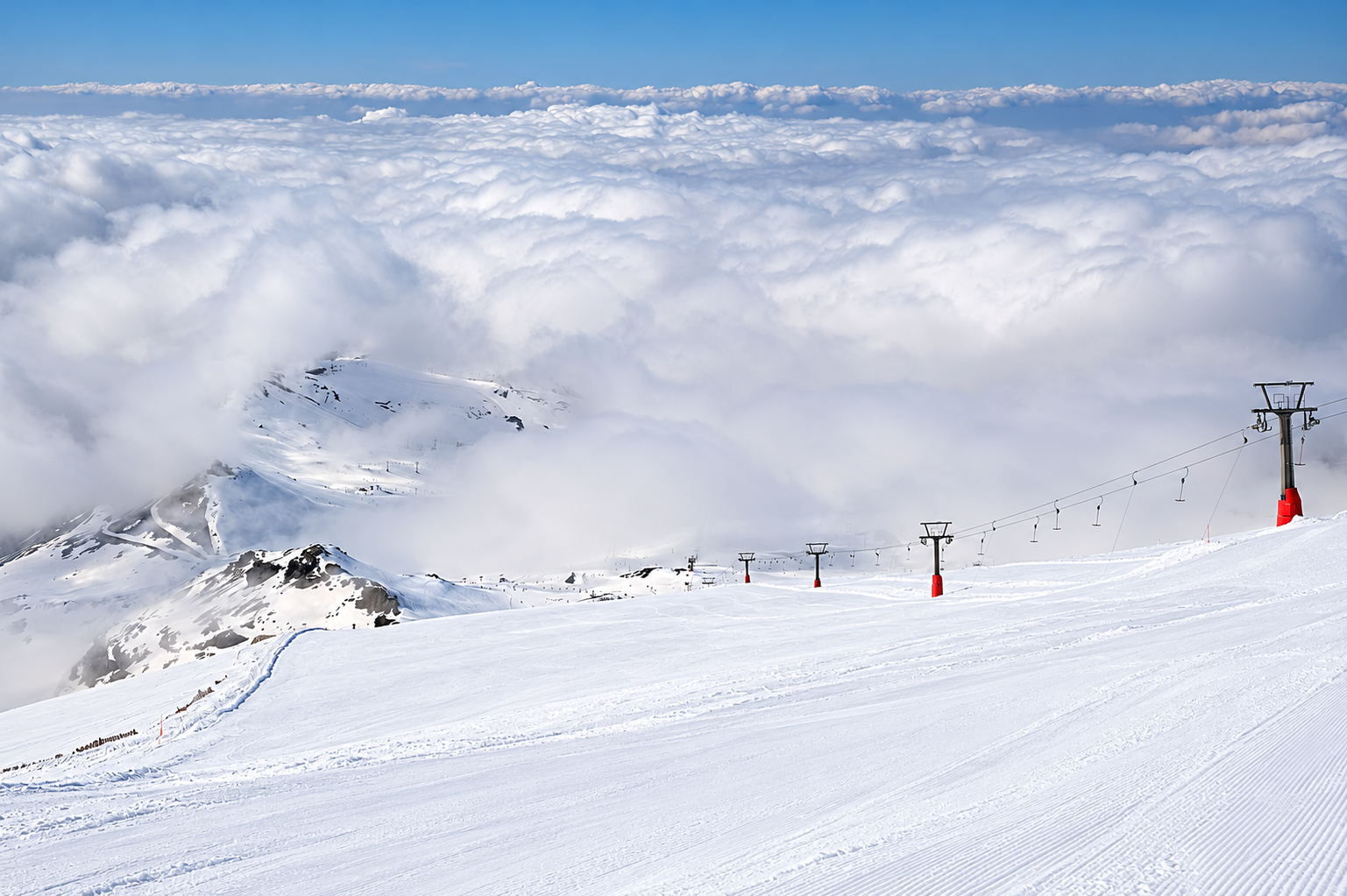 Snötäckta skidbackar och liftar i Sierra Nevada ovanför molnen.